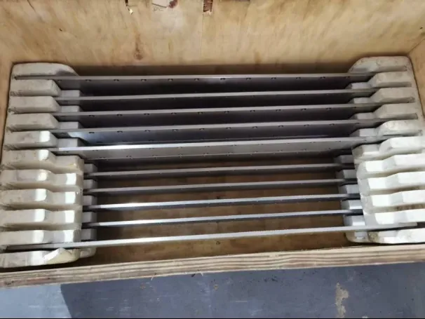 Long machined metal components neatly arranged in a wooden crate with protective foam inserts, ready for shipment