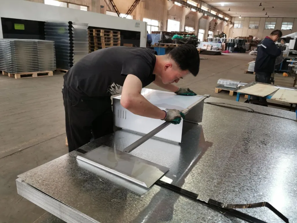 Worker performing sheet metal welding in a metal fabrication workshop with industrial welding equipment